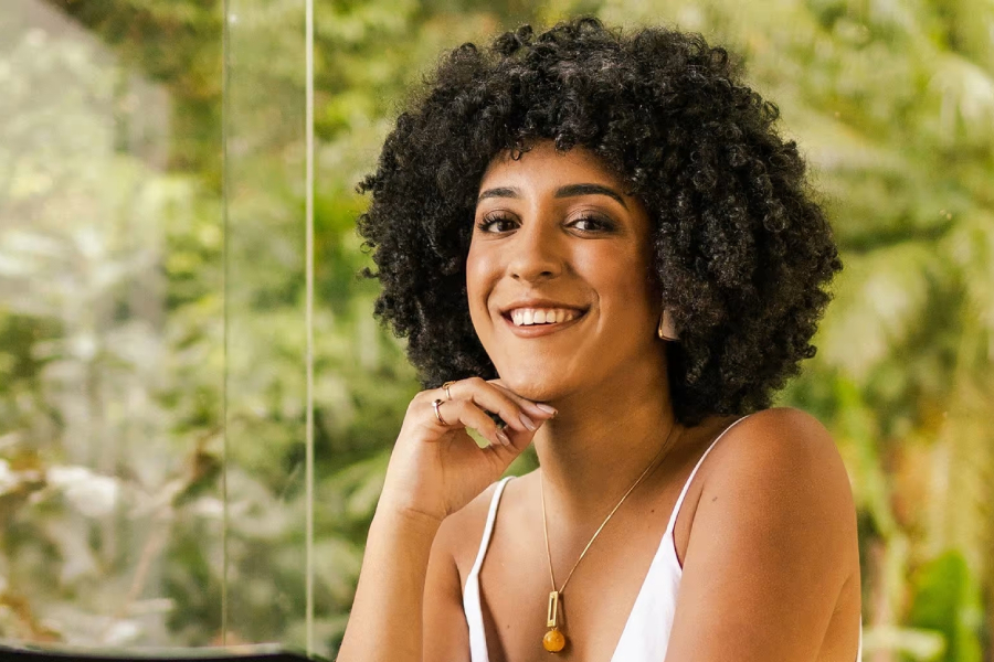 Nathalia Rodrigues é uma jovem negra de cabelo black power escuro e curto. Ela veste uma regata branca, usa maquiagem simples e está com a mão levemente encostada no queixo.